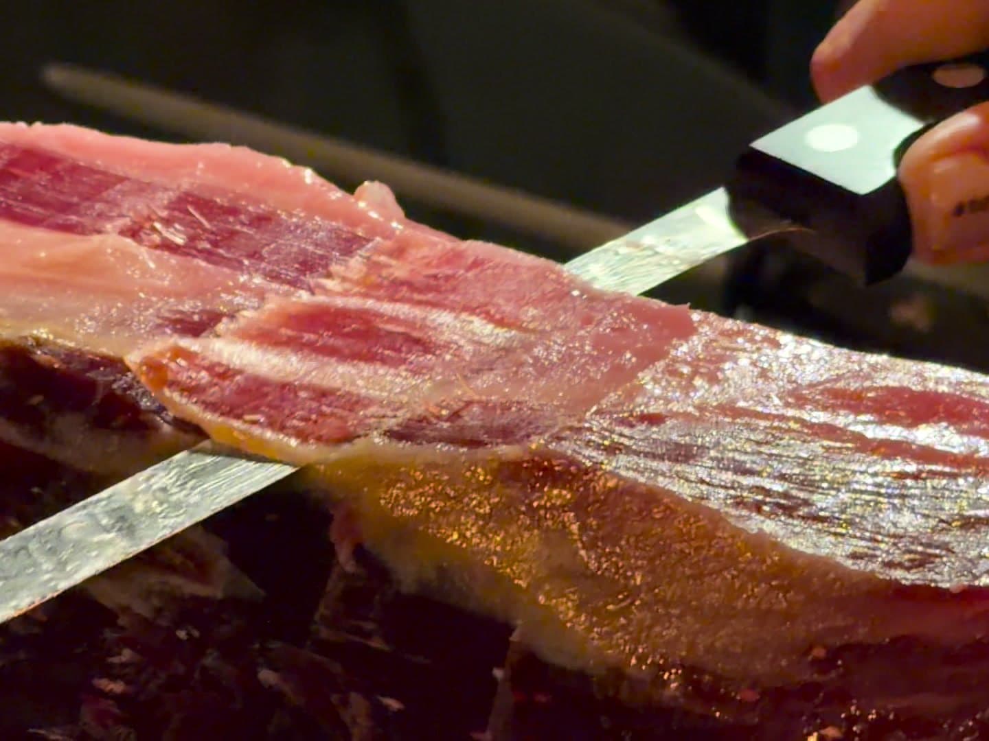 Cuchillo jamonero cortando lonchas finas de jamón ibérico