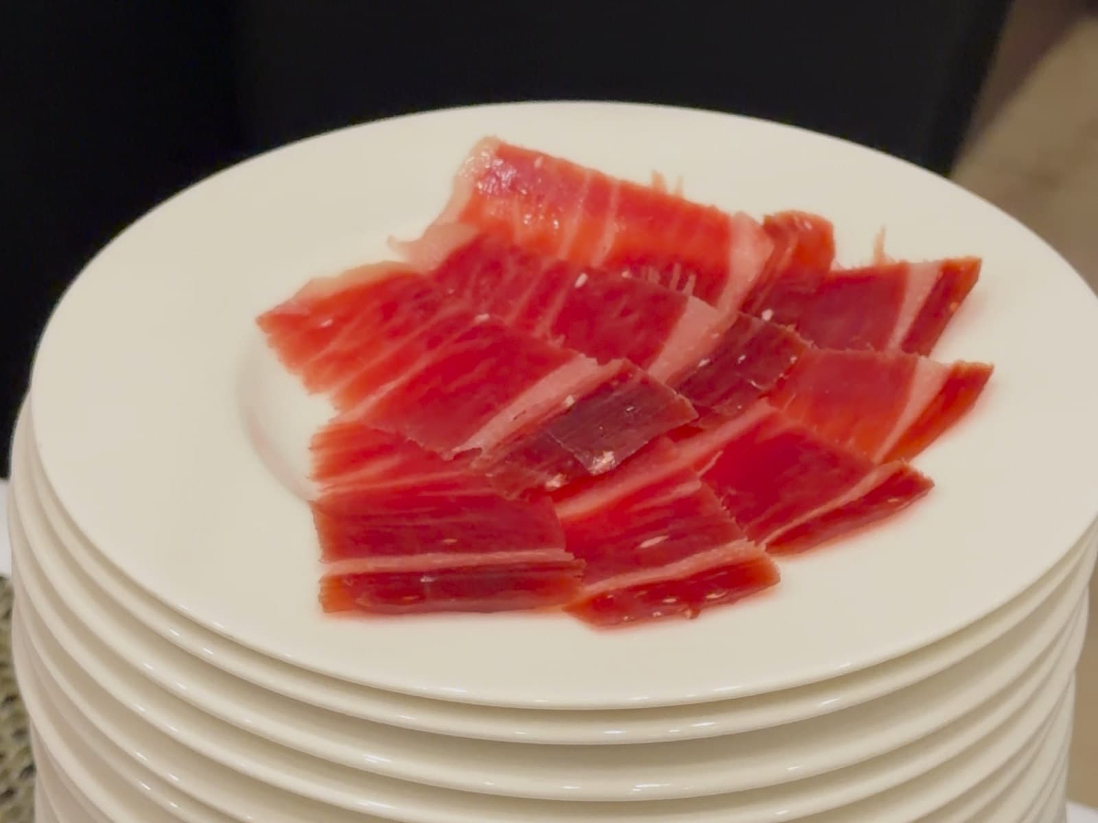 Un plato de lonchas de jamón de bellota 100 % ibérico recién cortadas, extendidas en una sola capa sobre una pila de platos.