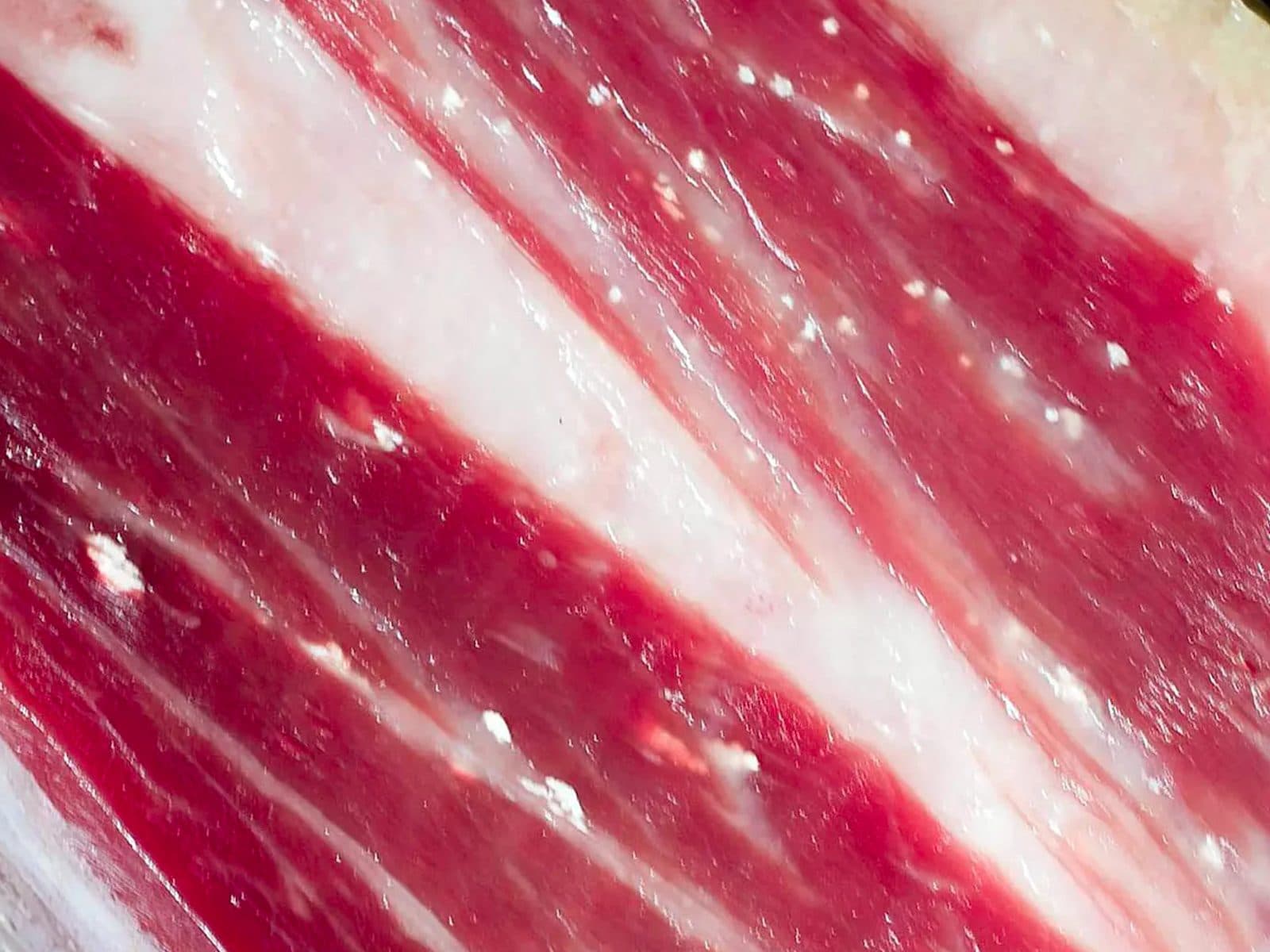 Cut surface of a cured ham with small white tyrosine crystals scattered through the lean meat, between the streaks of fat.