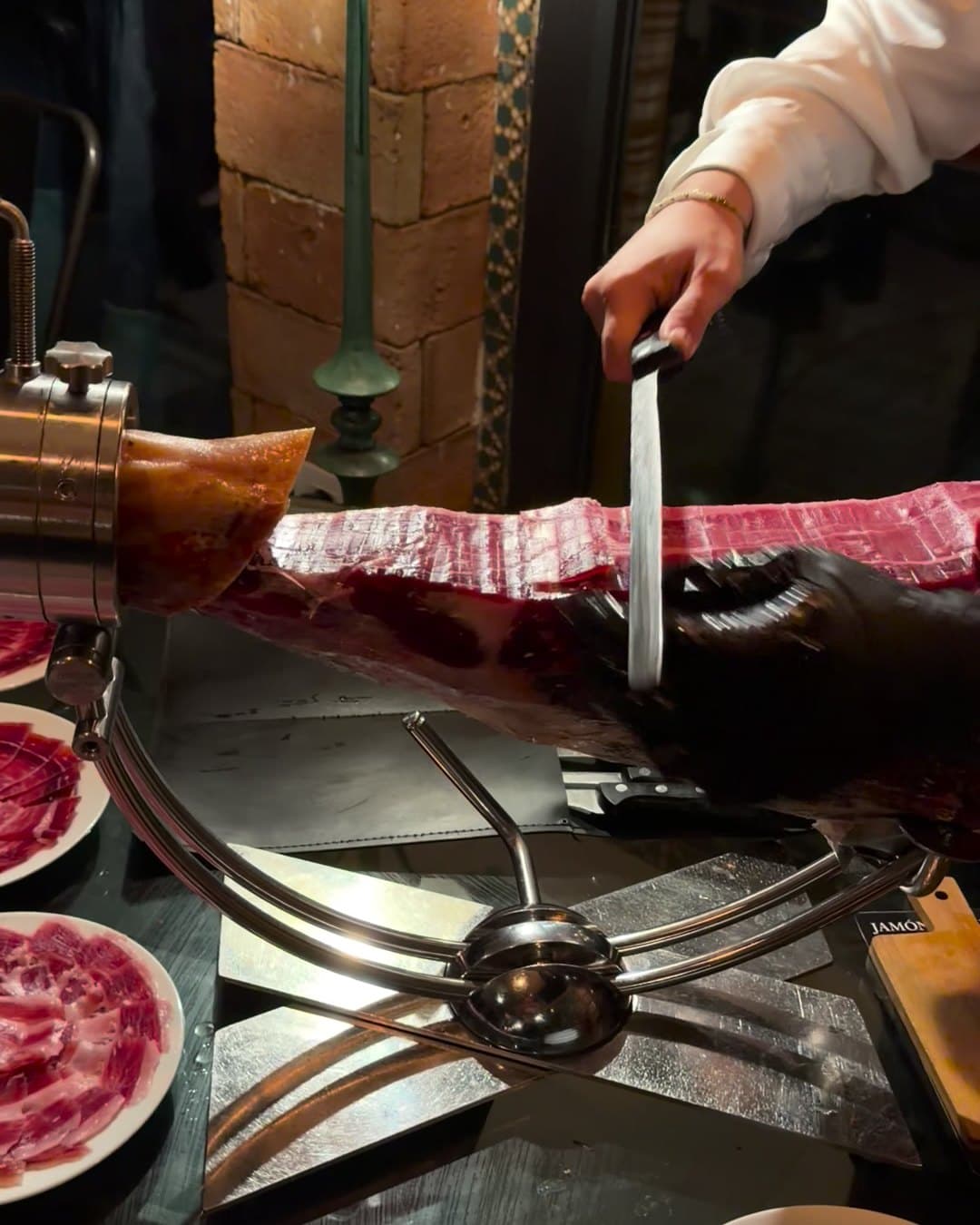 Corte a cuchillo de un jamón en el jamonero, con una pared de ladrillo al fondo